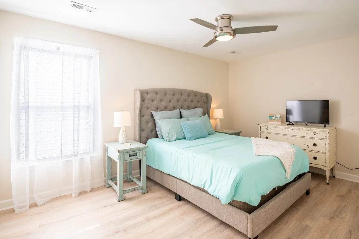 A tranquil bedroom featuring a bed with a tufted headboard, cozy nightstands with lamps, and a television. The space is softly lit, offering a relaxing atmosphere perfect for both quiet mornings and intimate evenings.