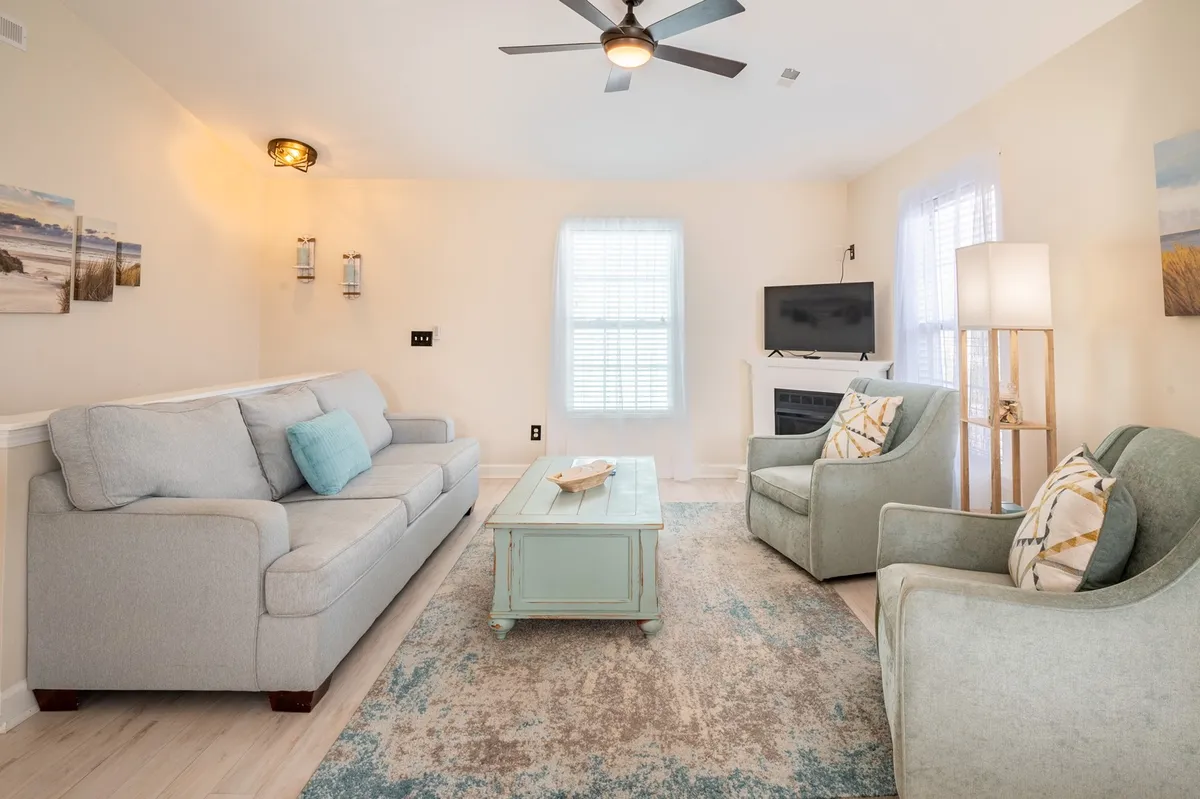 This interior living area features a light blue sofa, mint green coffee table, decorative pillows, and two accent chairs, with natural light filling the cozy space. The arrangement suggests a comfortable environment where guests and pets alike can unwind after a day of adventure.