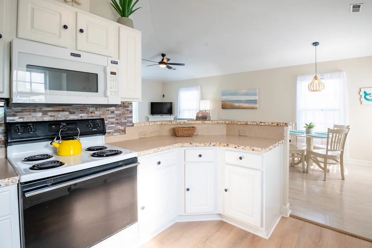 The image features a bright kitchen and dining area with modern appliances, a spacious countertop, and a table ready for shared meals. The open layout creates a welcoming atmosphere for cooking, dining, and socializing, ideal for group gatherings.
