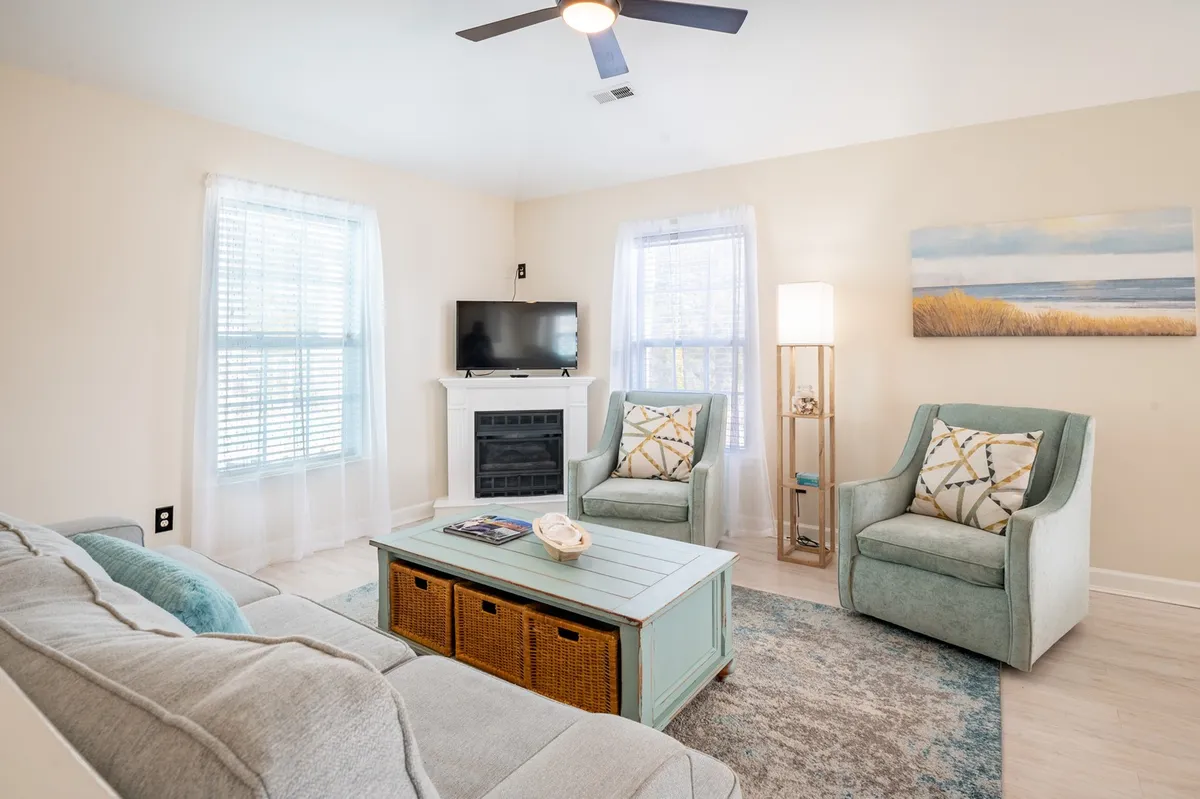 A living area highlighted by a comfortable sofa, decorative coffee table, two accent chairs, a television, and a cozy fireplace. The arrangement welcomes relaxation, conversation, or movie nights in a bright and appealing setting.