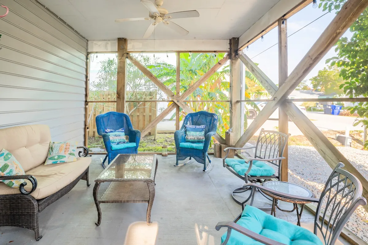 Close-up of a cheerful porch seating area featuring blue wicker chairs, a glass-top coffee table, and lush green plants in the background. The setup is ideal for conversation, drinks, or enjoying a book, exuding a welcoming and relaxing mood.