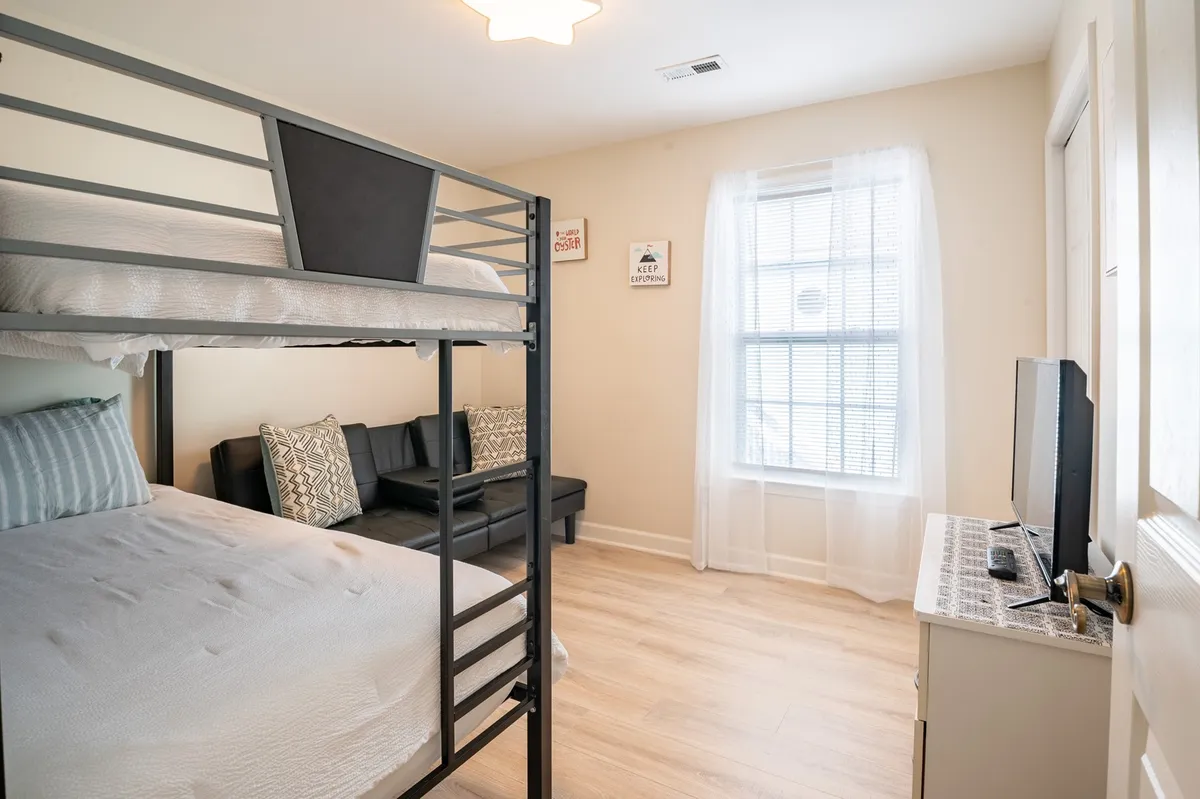 A cheerful kids' bunk room with a bunk bed and sofa, complemented by a window with sheer curtains. The setup encourages both play and relaxation, making it ideal for children or families.